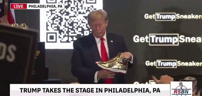 Trump holding up a pair of hideous gold TRUMP basketball shoes